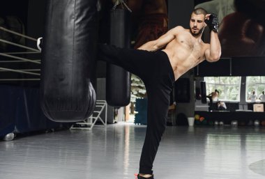 Dövüşçü Kum Torbasıyla Tekme Antrenmanı yapıyor. Koyu arkaplanda tekme, kum torbası. Spor salonunda siyah kum torbası tartılır.