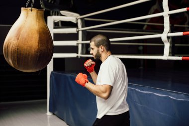 Dövüşçü Kum Torbasıyla Tekme Antrenmanı yapıyor. Koyu arkaplanda tekme, kum torbası. Spor salonunda siyah kum torbası tartılır.