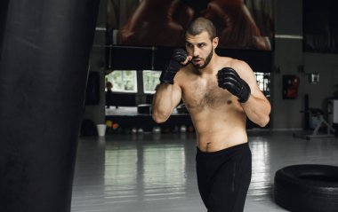 Dövüşçü Kum Torbasıyla Tekme Antrenmanı yapıyor. Koyu arkaplanda tekme, kum torbası. Spor salonunda siyah kum torbası tartılır.