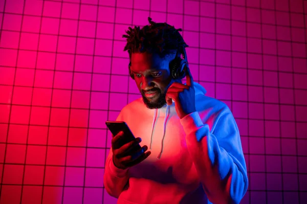 Koncepcja muzyki. Czarny człowiek słucha muzyki ze słuchawkami na tle neonowego światła. Czerwone i niebieskie tło — Zdjęcie stockowe
