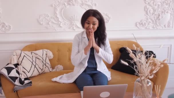 Friendly female black clinician in white gown using laptop for remote patient consultation in hospital office. Telemedicine. Online doctor appointment. — Stock Video