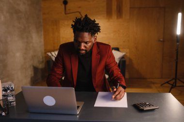 Yakışıklı siyahi adam rahat oturma odasında masa başında otururken dizüstü bilgisayarda çalışıyor. Evden Çalışan Bağımsız