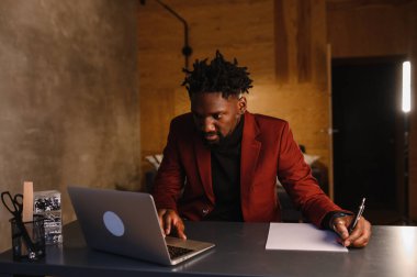 Ev işleri yapan yakışıklı siyahi Amerikalı adam oturma odasında bir koltukta otururken bilgisayarında video görüşmesi yapıyor.