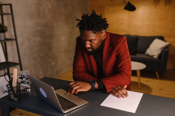 Homem negro afro-americano bonito trabalhando em casa e tendo chamada de vídeo no computador portátil enquanto sentado em um sofá na sala de estar — Fotografia de Stock