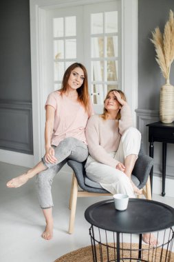 Kanepede oturmuş heyecanlı bir şekilde konuşan, gülümseyen iki çekici kız arkadaş.