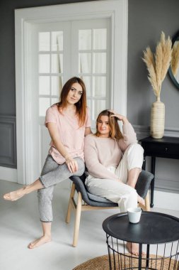 Kanepede oturmuş heyecanlı bir şekilde konuşan, gülümseyen iki çekici kız arkadaş.