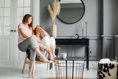 Kanepede oturmuş heyecanlı bir şekilde konuşan, gülümseyen iki çekici kız arkadaş.