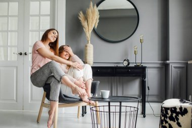 Kanepede oturmuş heyecanlı bir şekilde konuşan, gülümseyen iki çekici kız arkadaş.