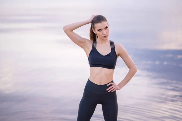 Retrato de un hermoso modelo de fitness sobre un fondo del mar al atardecer — Foto de Stock