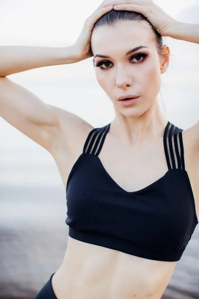 Atletisk flicka med tank top gör en sträcka på stranden — Stockfoto