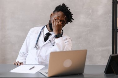 İş yerinde sıkılmış Afrikalı Amerikalı doktor ofis masasında uyuyakalıyor, işyerinde uyuyan çalışanlar dizüstü bilgisayarın yanında aşırı çalışılmış hissediyorlar.