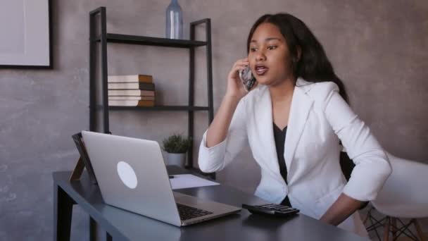 Sorrindo jovem mulher de negócios afro-americana trabalhando em um laptop em sua mesa em um escritório moderno brilhante — Vídeo de Stock