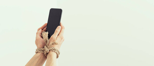 Руки связаны верёвкой на белом фоне, что предполагает интернет-зависимость или зависимость от социальных сетей