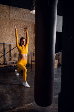 Sarı eşofmanlı güzel bir kız esneme hareketleri yapıyor. Geniş pencereli modern spor salonu