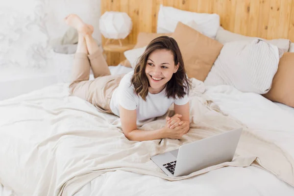 Une jeune fille séduisante est allongée au lit et vérifie les réseaux sociaux. Appartement lumineux moderne — Photo