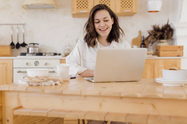 Happy millennial Kaukasische vrouw zitten aan tafel werken online op laptop te raadplegen client op het web. Lachende jonge studente studeert op afstand op de computer. E-learning-concept. — Stockfoto