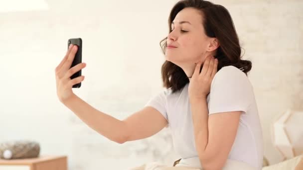 Close-up van een opgewonden vrouw die lacht, een smartphone vasthoudt, een selfie maakt, plezier heeft met een gadget, op bed ligt en geniet van haar vrije tijd — Stockvideo