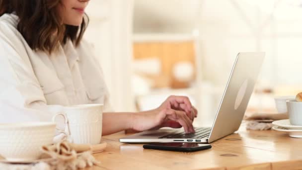 Close-up van een meisje dat aan een laptop werkt, tekst typt. Op tafel ligt een laptop en een telefoon. Werk als freelancer of programmeur — Stockvideo