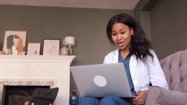 Médico negro fêmea amigável em vestido branco usando laptop para consulta remota paciente no escritório do hospital. Telemedicina. Consulta médica online. — Vídeo de Stock