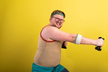 komik şişman adam dambıllarla egzersiz yapıyor. Fazla kilolu. sarı arkaplan