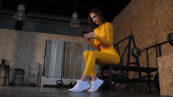 A young attractive woman in the gym sits and surfs the phone or communicates on social networks — Stock Video