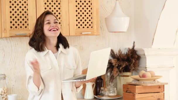 A young attractive woman in a bright modern kitchen uses a laptop for video communication — Stock Video