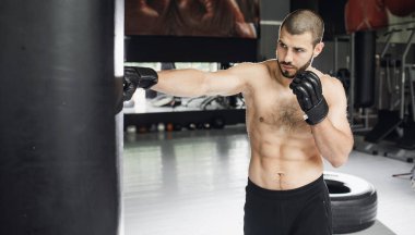 Dövüşçü Kum Torbasıyla Tekme Antrenmanı yapıyor. Koyu arkaplanda tekme, kum torbası. Spor salonunda siyah kum torbası tartılır.