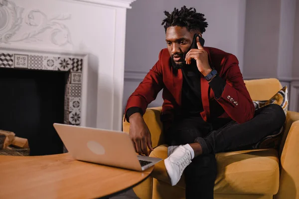 Sorrindo milenar homem casual afro-americano trabalhando com aplicativos ou se comunicando on-line no laptop — Fotografia de Stock