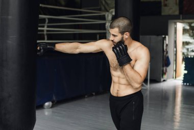 Dövüşçü Kum Torbasıyla Tekme Antrenmanı yapıyor. Koyu arkaplanda tekme, kum torbası. Spor salonunda siyah kum torbası tartılır.