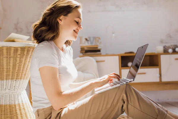 Een jonge aantrekkelijke vrouw in een licht modern appartement gebruikt een laptop om online te communiceren of te studeren — Stockfoto