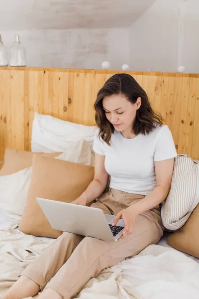 Γυναίκα χαλαρώνοντας στο κρεβάτι χρησιμοποιώντας φορητό υπολογιστή για βιντεοκλήση σε μοντέρνο επίπεδο — Φωτογραφία Αρχείου