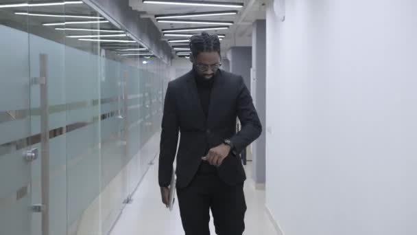 Empresario africano enfocado caminando en la reunión en la oficina. Gerente afroamericano caminando por el pasillo de oficinas. Primer plano hombre de negocios afro serio va a la reunión en el centro de negocios. — Vídeo de stock