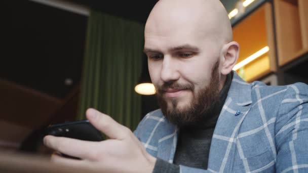 Homem de negócios em um terno sentado em um café trabalha em um laptop e surfa o telefone — Vídeo de Stock