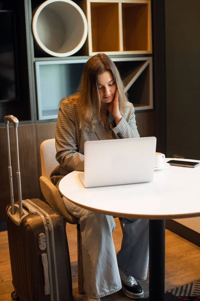 Een jong aantrekkelijk mollig meisje zit in een cafe drinken koffie en werken op een laptop — Stockfoto