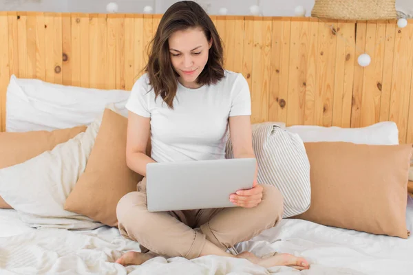 Jong aantrekkelijk meisje, maakt gebruik van een laptop in bed. Werk op afstand van huis — Stockfoto