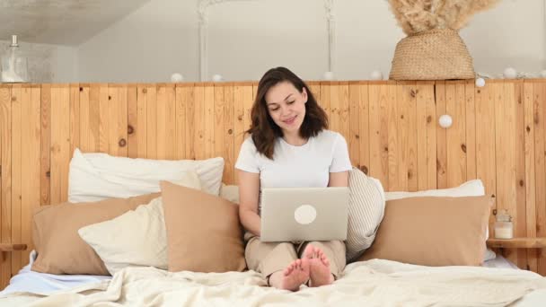 Jong aantrekkelijk meisje, maakt gebruik van een laptop in bed. Werk op afstand van huis — Stockvideo