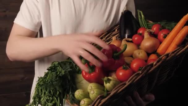 Egy boldog farmer fehér pólóban és kalapban egy kosár friss gyümölcsöt és zöldséget tart — Stock videók