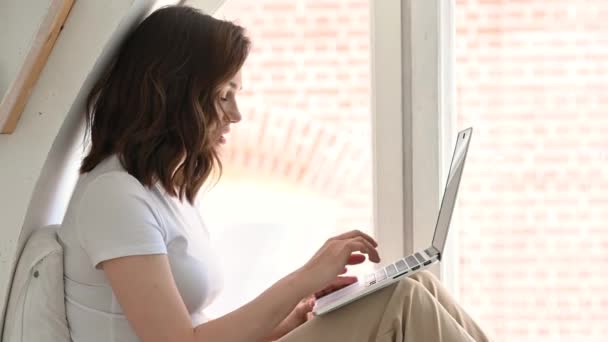 Fiatal vonzó lány az ő fényes lakás, élvezi a reggelt egy laptop használatával. A közösségi hálózatok ellenőrzése — Stock videók