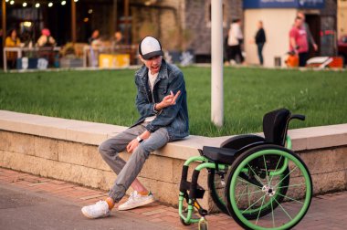 Genç engelli bir adam tekerlekli sandalyenin yanına oturur ve ona orta parmağı gösterir.