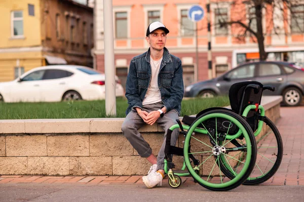 Mladý muž se zdravotním postižením sedí na lavičce vedle invalidního vozíku — Stock fotografie
