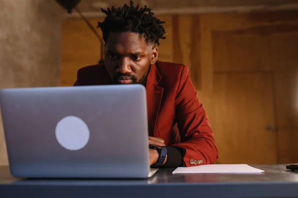 Um negro focado num fato está a trabalhar num portátil. Trabalho remoto em casa — Fotografia de Stock