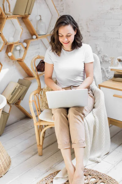 Een jonge aantrekkelijke vrouw in een licht modern appartement gebruikt een laptop om online te communiceren of te studeren — Stockfoto
