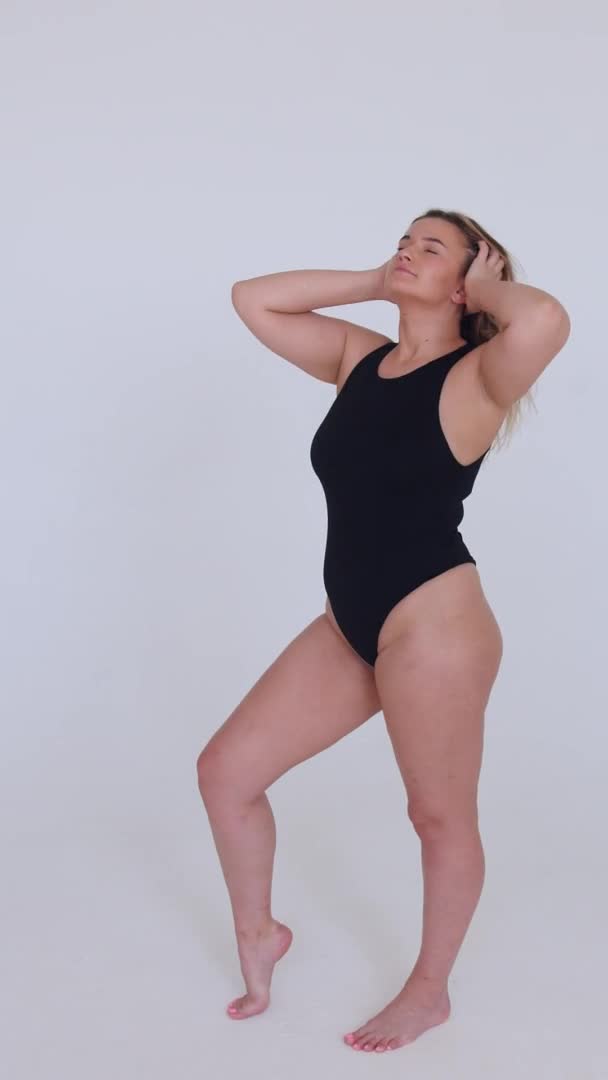Beautiful overweight woman in black swimsuit on white background. Vertical video — Stock Video