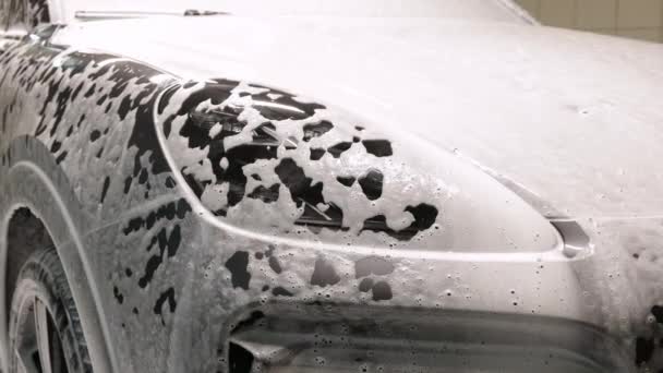 Mașină de curățat cu șampon cu spumă albă de zăpadă. Pulverizarea spumei albe de zăpadă pe capota mașinii și farurile. Pulverizarea spumei de șampon auto pe capota mașinii — Videoclip de stoc