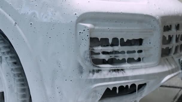 Sprzątanie samochodu z białym szamponem z pianki śnieżnej. Rozpylanie białej śnieżnej pianki na maskę samochodu i reflektor. Spray samochód szampon pianka do maski samochodowej — Wideo stockowe