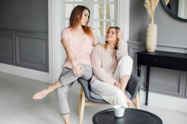 Kanepede oturmuş heyecanlı bir şekilde konuşan, gülümseyen iki çekici kız arkadaş.