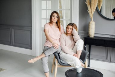 Kanepede oturmuş heyecanlı bir şekilde konuşan, gülümseyen iki çekici kız arkadaş.