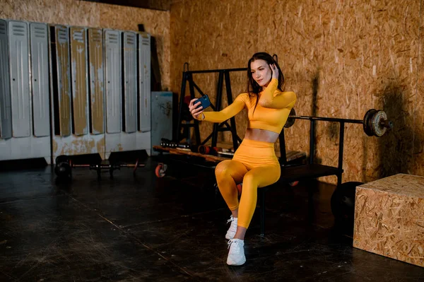 Молода спортивна дівчина в жовтій спортивній формі готується до тренування. Сучасний тренажерний зал в стилі лофт — стокове фото