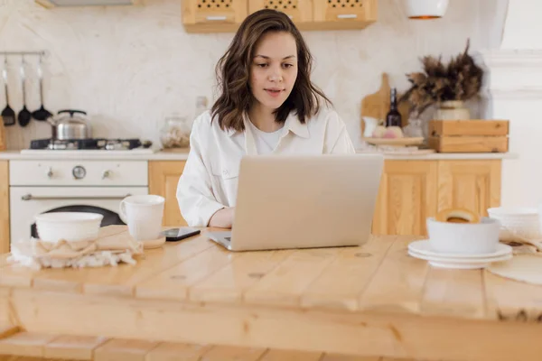 Aantrekkelijke vrouw die werkt op een laptop zittend aan een bureau in een gezellige woonkamer. Zakenvrouw zitten op de werkplek, tekst op de computer hebben drukke vruchtbare dag op kantoor — Stockfoto