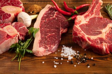 Ahşap bir masada çiğ et parçaları. Biber, sarımsak, baharat.